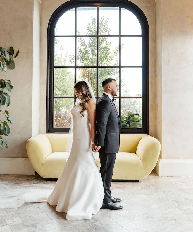 Bride and groom standing back to back holding hands for their private vows before their black-and-white wedding.