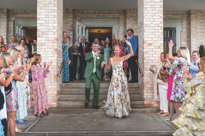 Bride and groom walking out of venue  while guests cheer around them.