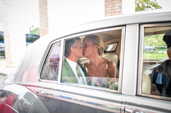 Newlyweds kissing in the back of getaway car.