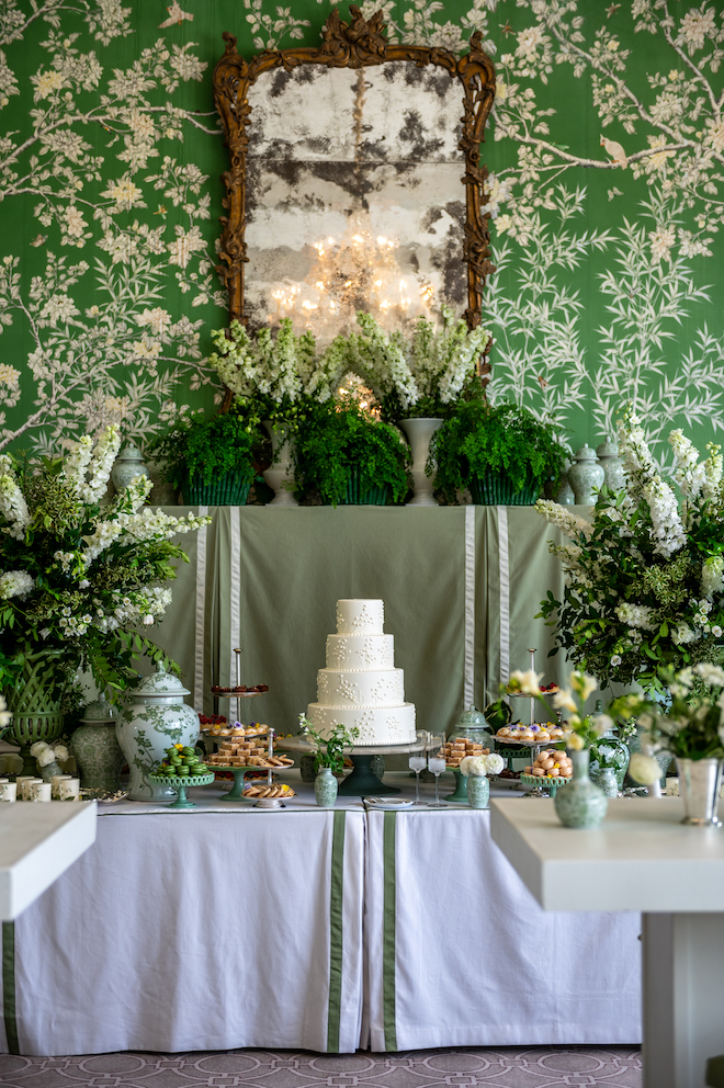 Four tier classic white wedding cake surrounded by green details and mini brunch bites for inspo to plan your perfect wedding.
