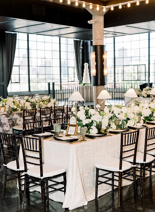 White flowers, greenery and lamps decorate the reception tables at their emerald green wedding. 