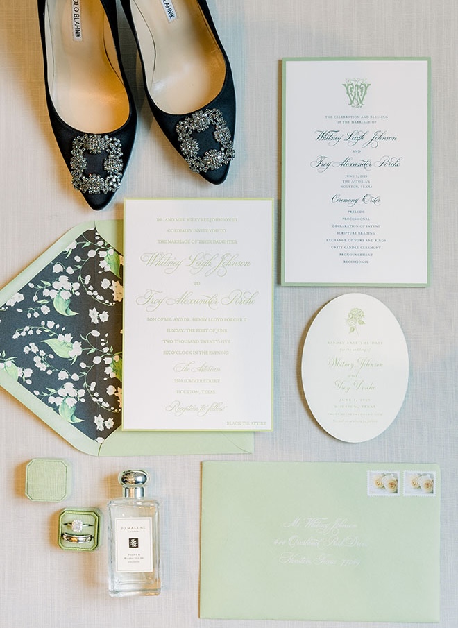 Green wedding stationery and invitations are placed next to the brides shoes and accessories. 