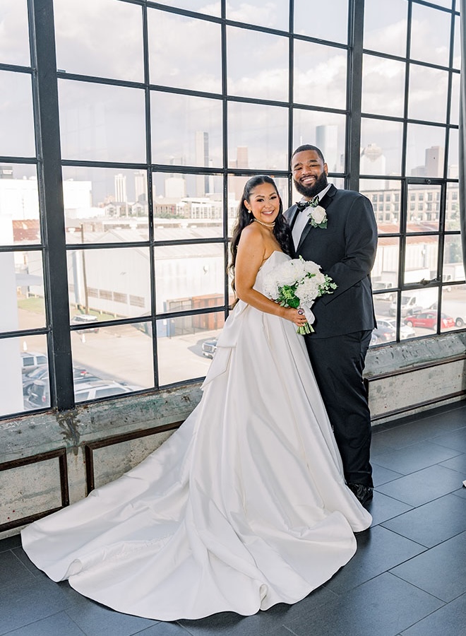 The bride and groom stand in front of the window at The Astorian that overlooks downtown Houston. 