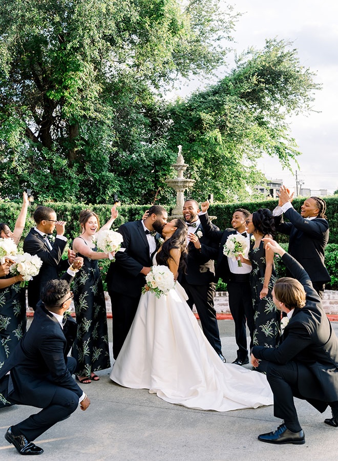 The bride and groom share a kiss as their wedding party cheers around them.