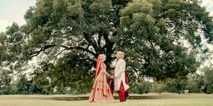 Bride and groom hold hands aside an oak tree at their indian fusion wedding at Hyatt Regency Lost Pines Resort