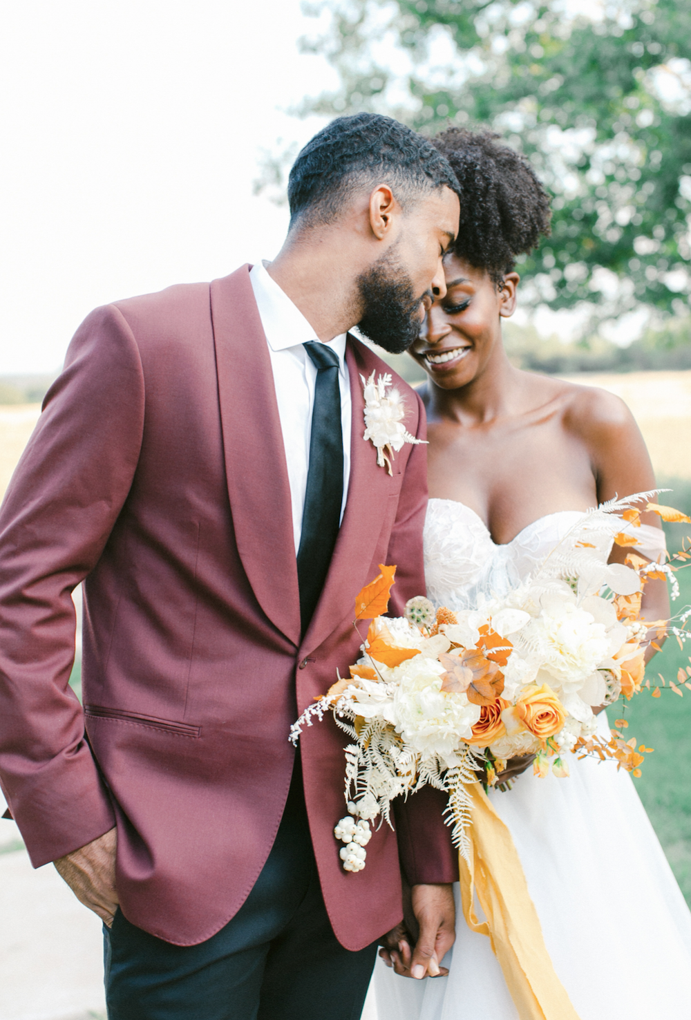 Bride holding bouquet and groom in maroon suit embracing.